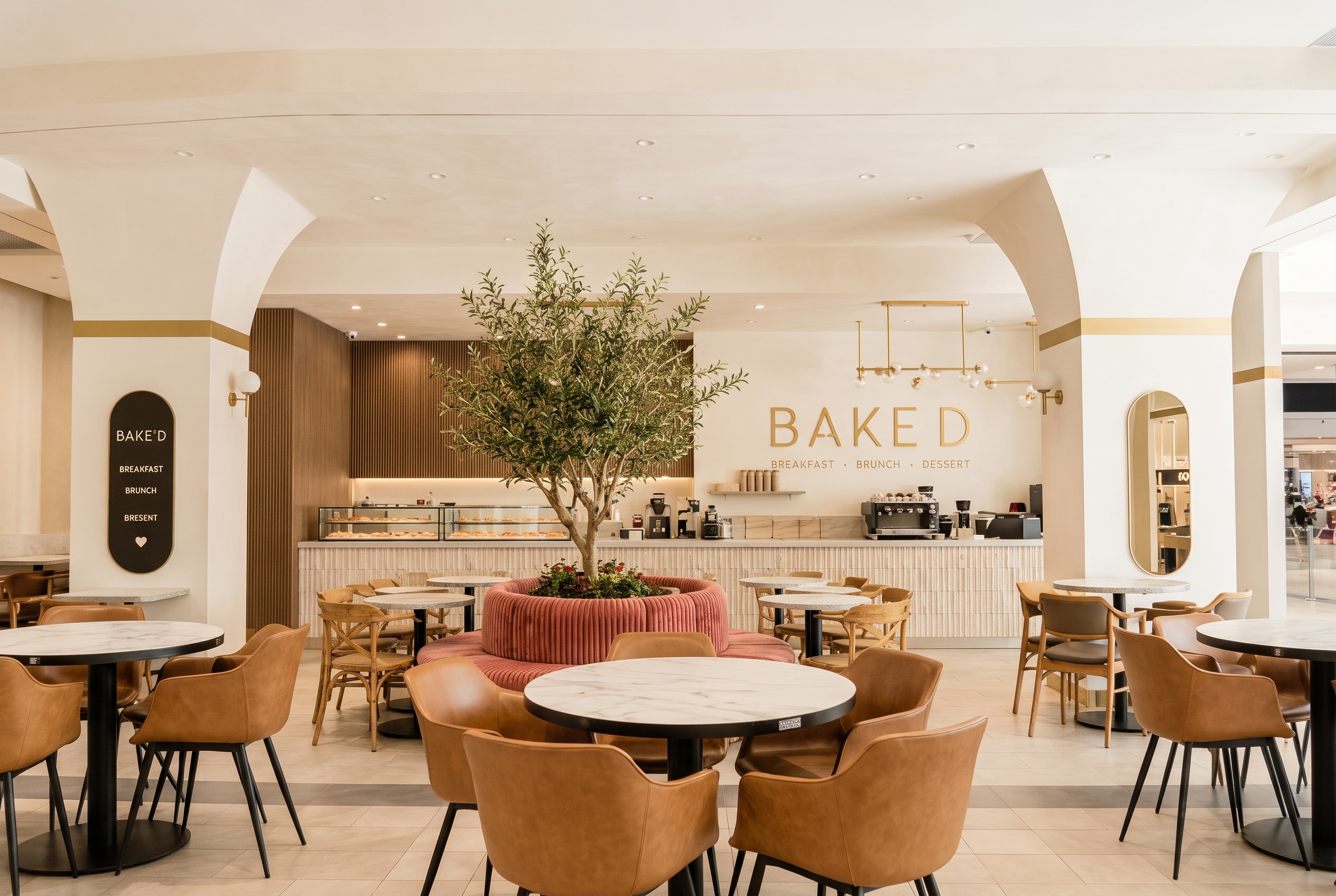 Inside a BAKED cafe: an olive tree, pink velvet banquette and gold BAKED signage